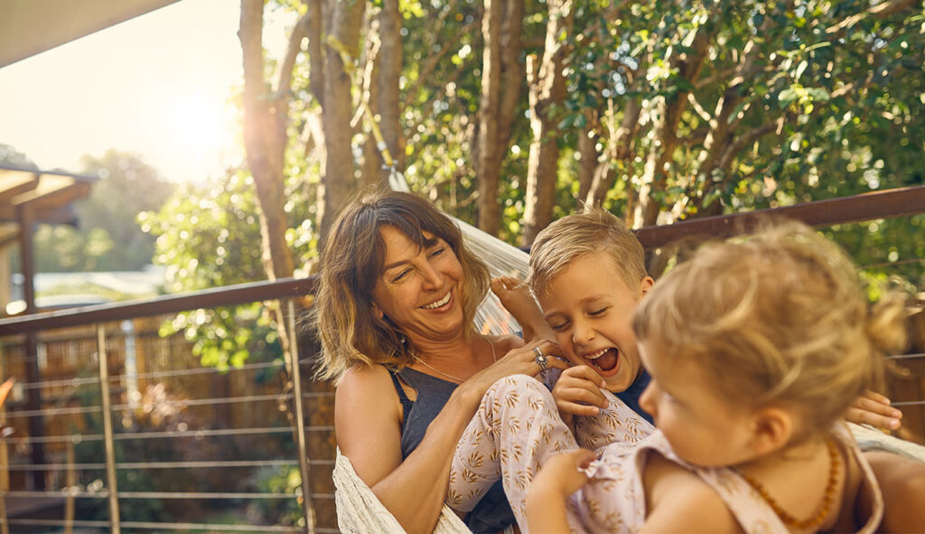 Mother relaxing in a hammock with her two young children on a sunny afternoon.