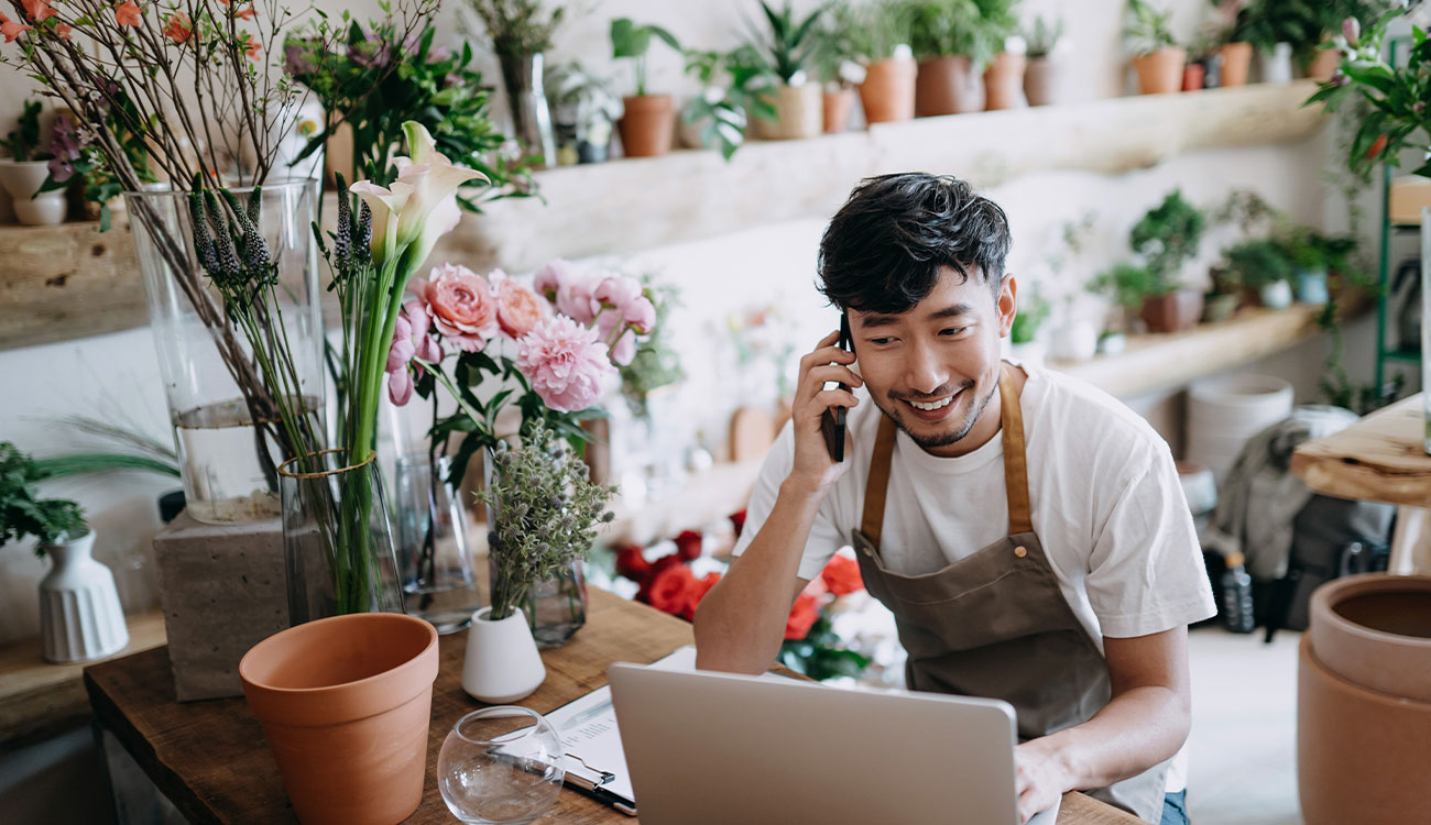 A small business owner working in a flower shop, managing calls and online tasks, representing the needs of local businesses supported through business and community banking.