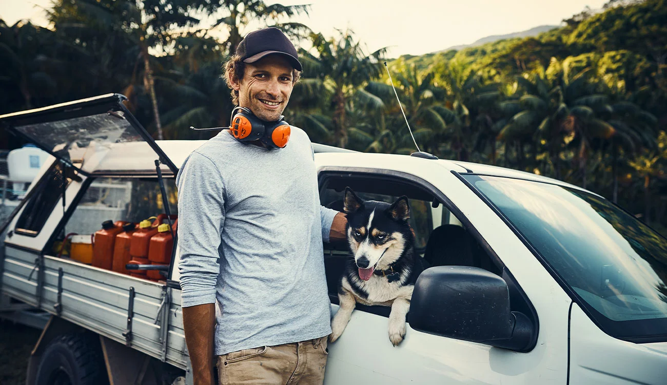 A man standing beside his work ute with his dog, representing business vehicle use