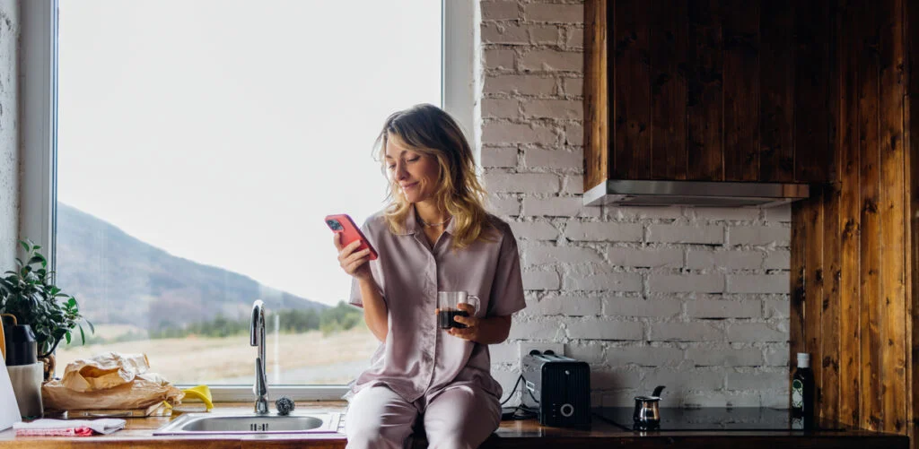 A Happy Beautiful Blonde Businesswoman In Pajamas Texting On Her Mobile Phone While Relaxing At Home In The Morning