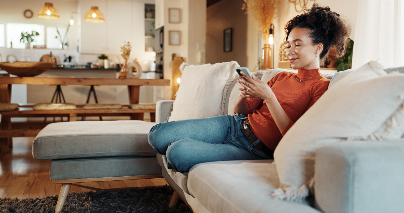 Visa Click to Pay | Summerland Bank | House, relax and woman with smartphone, typing and connection with smile, app and social media. Apartment, person and girl on couch, cellphone and mobile user with internet, online game and network